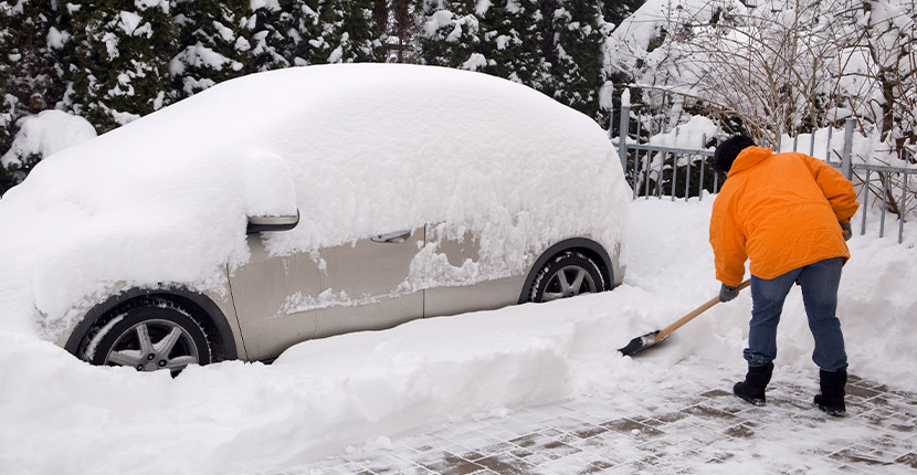 Person in an orange coat shoveling out a vehicle