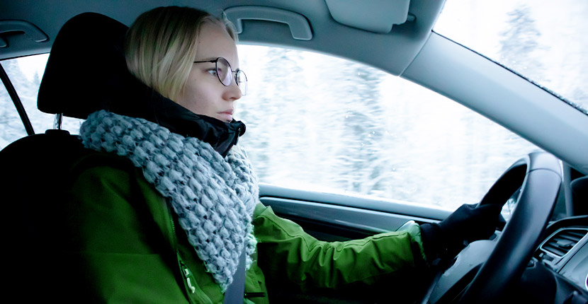 Woman in green coat and blue scarf driving in winter